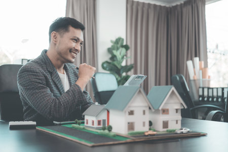 A group of young Asian businesspeople meet at an office for a residential real estate project. A group of elegant, professionally dressed individuals evaluate a small house model.の写真素材