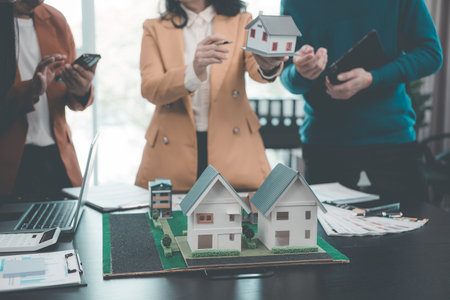 A group of young Asian businesspeople meet at an office for a residential real estate project. A group of elegant, professionally dressed individuals evaluate a small house model.の写真素材