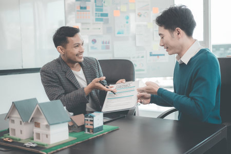 A group of young Asian businesspeople meet at an office for a residential real estate project. A group of elegant, professionally dressed individuals evaluate a small house model.の写真素材