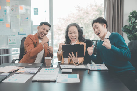Group of successful Asian businesspeople smiling and laughing, posing and making gestures of joy together in a company office conference room.の写真素材