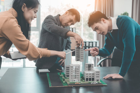 A group of young Asian businesspeople meet at an office for a residential real estate project. A group of elegant, professionally dressed individuals evaluate a small house model.の写真素材