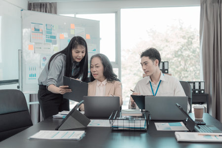 Group of business people discussing charts and graphs showing results of teamwork of colleagues working together at desks in office and discussing documents.の写真素材