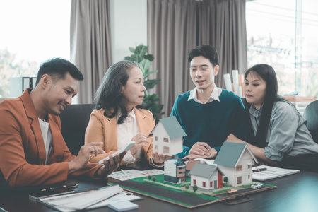 A group of young Asian businesspeople meet at an office for a residential real estate project. A group of elegant, professionally dressed individuals evaluate a small house model.の写真素材