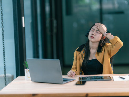 Asian call center woman is stressed from working with headphones, sitting and checking computer screen in the office.の写真素材
