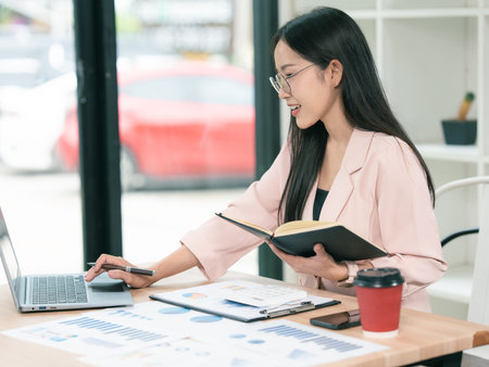 Beautiful Asian businesswoman working with computer and financial documents calculating analysis with laptop in office.の写真素材
