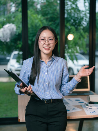 Beautiful Asian businesswoman holding clipboard and smiling at camera standing office working conceptの写真素材