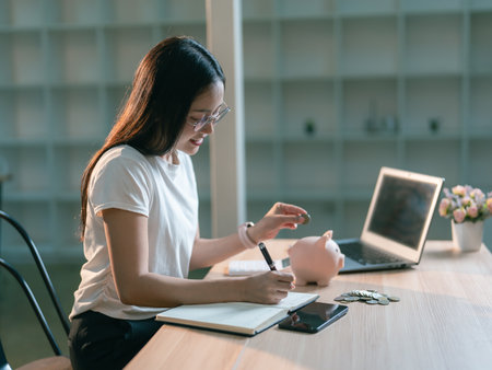 Asian woman putting coins into piggy bank to save money, financial planning for future use.の写真素材