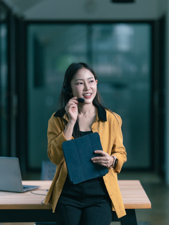 Beautiful Asian woman wearing headphones while working on laptop computer in office.の写真素材