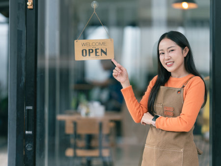 Young Asian woman in apron holding digital tablet in coffee shop. Barista, waitress smiling and looking into camera.の写真素材