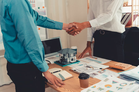 Businessmen shaking hands in front of real estate, symbolizing cooperation and successful deal. Close-up.の写真素材