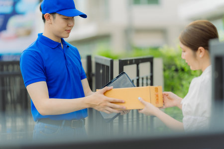 Delivery man wearing blue shirt is delivering packaged goods to young female customer at front door delivery conceptの写真素材