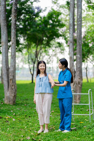 Asian nurse and elderly female patient standing in park and holding hands. Concept of care for...