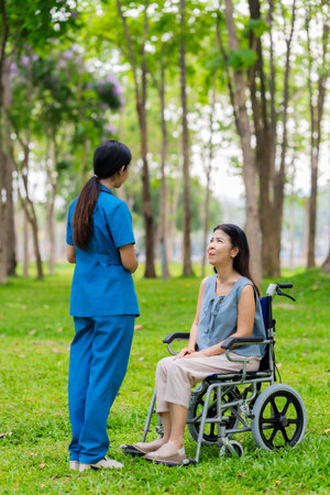 Asian female nurse assists and cares for elderly female patient sitting in wheelchair receiving physical therapy in nursing home park. Health concept.の写真素材