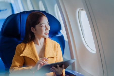 Asian woman using digital tablet while traveling by plane. Female passenger using digital device in...