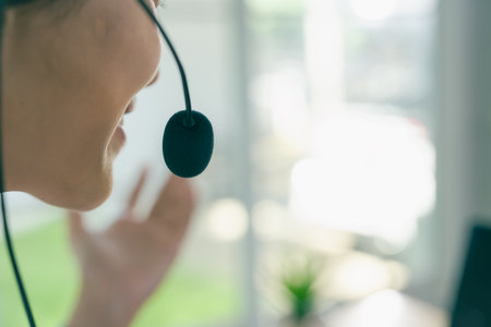 An Asian woman, a call center employee, wears headphones, works from home, communicates via headphones, and provides professional online support.の写真素材