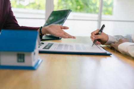 A real estate agent or broker is showing a house plan to a client. The plan includes a pen, and they are discussing contract details with the client during a meeting in the office.の写真素材
