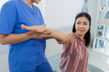 An Asian female physiotherapist is performing physical therapy on an elderly patient in a hospital to help with muscle rehabilitation.の写真素材