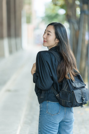 A woman is walking along a city street with a smartphone and a backpack, posing with the city...