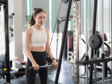 A fit Asian woman is working out with strength training ropes in a gym. Muscle-building workouts at...