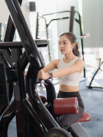 A beautiful Asian woman is working out in the gym, showcasing her strength and physical fitness for...