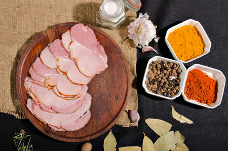 the photograph shows some pieces of ham cut into slices on top of a wooden board with some pieces of bread and some spicesの写真素材