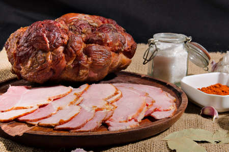 The photograph shows a piece of smoked ham next to sliced ham on a wooden boardの写真素材