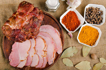 The photograph shows a piece of smoked ham next to sliced ham on a wooden boardの写真素材
