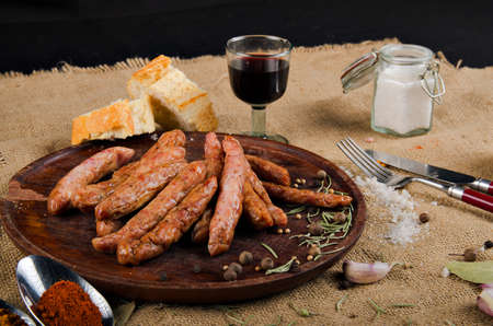 The photograph shows many salami on a wooden board next to a piece of bread, cutlery and some spices.の写真素材