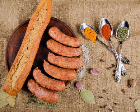 The photograph shows many sausages on a wooden board next to a piece of bread, cutlery and some spices.の写真素材