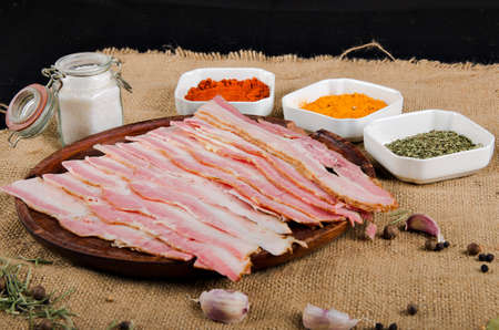 the photograph shows some pieces of bacon on a wooden board with some spicesの写真素材