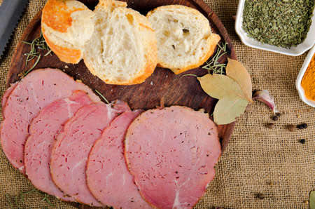 the photograph shows some pieces of ham cut into slices on top of a wooden board with some pieces of bread and some spicesの写真素材