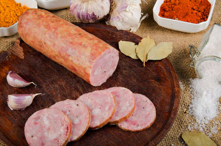The photograph shows a quite appetizing salami, sliced on top of a wooden board with some spices.の写真素材