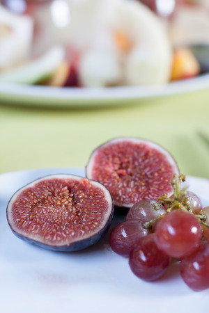 Two figs and grapes on white plate and green tablecloth with blurred fruits on backgroundの写真素材