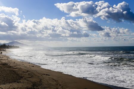 Turquoise sea with several martens flying over it and mountains on backgrdound with dark grey skyの写真素材