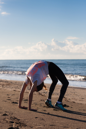 Young woman in crab posture on beach wearing black tights and white top with pink letters on itの写真素材
