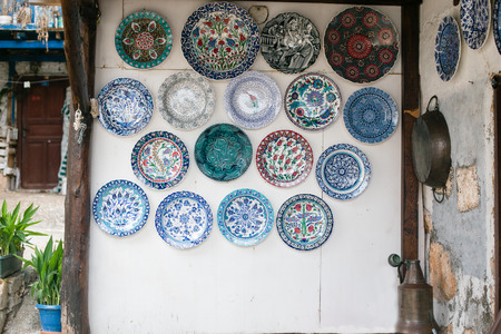 White wall decorated with many ceramic plates in blue and turquoise tones with plants in pots on left side and iron tray hangin on wall on right sideの写真素材