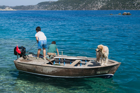 SIMENA, TURKEY - MAY 20 Two boys in wooden boat and dog in bay of Uchagiz in Antalya province in Turkey with turqouise sea and mountian on background 2016のeditorial素材