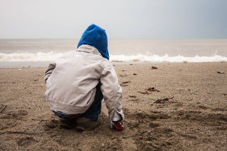 Portrait of toddler boy sitting and playing at  beach on gloomy dayの写真素材
