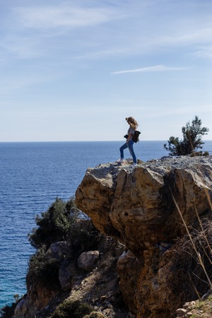 Blond woman photographer enjoying seaview and standing on high rock cliff portrait layoutの写真素材