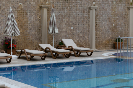 Three brown sunbeds with biege matresses and two striped umbrellas against mosaic wall with columnsの写真素材