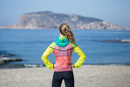 Healthy and fitness lifestyle Back view portrait of young woman standing on beach in gym clothing with sea and Alanya castle backgroundの写真素材