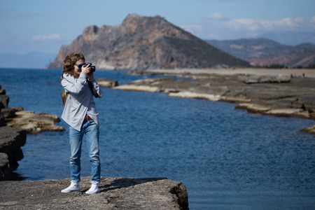 Young woman wearing jeans gray jacket and backpack standing and photographing rock ribbed beach in Gazipasha Alanya Turkey famous for its lagoonsの写真素材