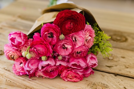 Bouquet of several pink and one  drak red ranunculus wrapped in craft paper lying on wooden rustic...