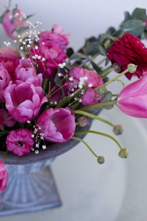 pink ranunculus and pink tulips arrangement in iron vase  over light backgroundの写真素材