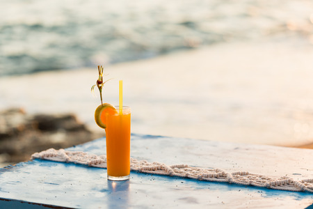 Glass of fresh orange juice over blue tabletop with sea and beach on backgroundの写真素材