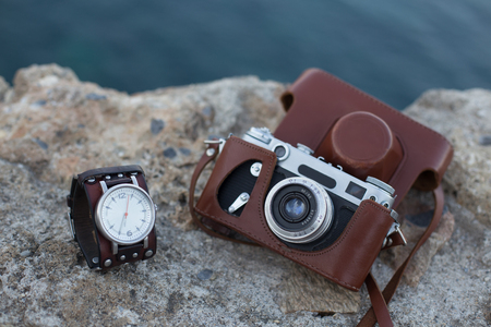 Old vintage film camera in brown leather case and watch with leather bracelet placed on stone  surfaceの写真素材