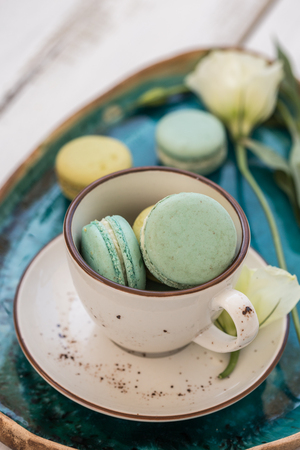 Flat turquoise ceramic plate with a cup,p5 green macaroons and white lisianthus, placed over white rustic tabletopの写真素材
