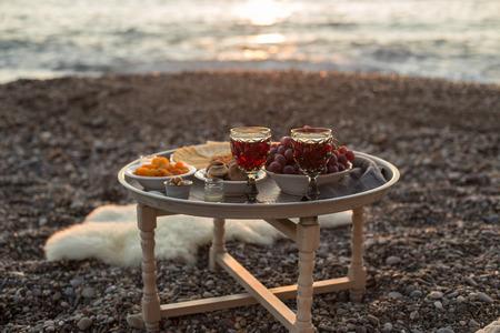 Romantic outdoor dinner with wine and cheese by seaside. Two glasses of wine, grapes, olives and...