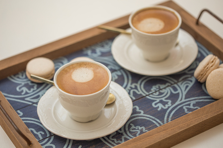 two cups of coffee with vanilla macaroons in a wooden trayの写真素材