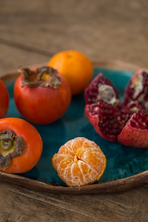 Tangerine, persimmon and pomegranate in a turquoise ceramic plate with tangerine in sharp focus and...